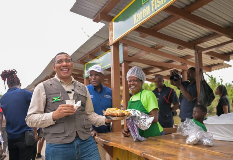 Photo by: Yhomo Hutchinson Prime Minister, Dr. the Most Hon. Andrew Holness (left), laughs as he is presented with a large container of fried fish by a vendor at the reopening of shops in Border, St. Elizabeth on January 16. Sharing in the moment is Minister of Industry, Investment and Commerce, Senator the Hon. Aubyn Hill.