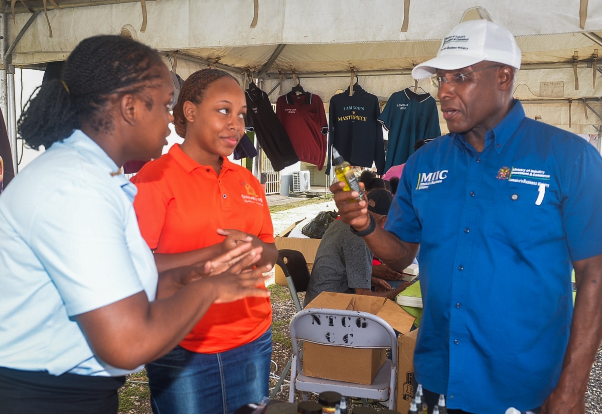 Minister of Industry, Investment and Commerce, Senator the Hon. Aubyn Hill (right) looks at a product, as Founder of Go4theKD’sglow, Keisha Dunkley (left) provides information, during the New Testament Church of God Kingdom Builders Business Expo, held in Old Harbour, St. Catherine, on Saturday (July 11). Joining the discussion was Tiana Clarke (center).